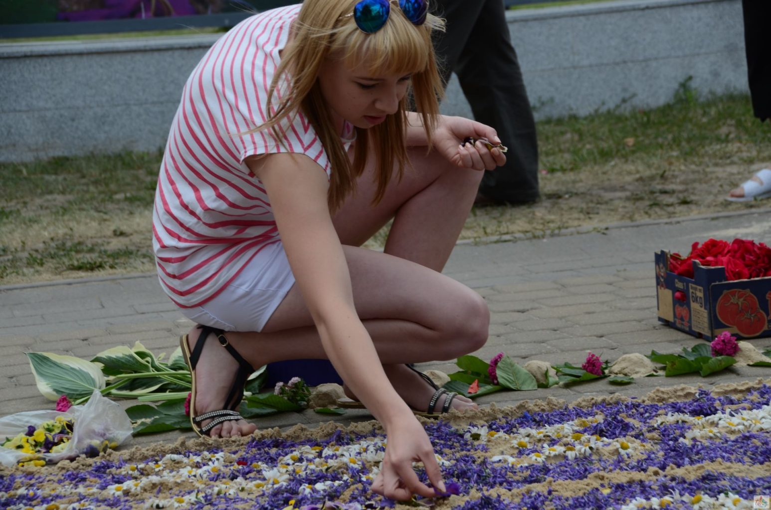 Dziewczyna układa na ziemi wzór z żywych kwiatów